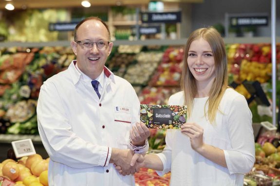 Manomama-Wettbewerb-Gewinnerin Luisa Dick erhält von Kaufmann Ingo Müller ihren Einkaufsgutschein